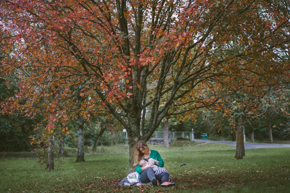 donna che tiene il bambino seduto sotto l'albero