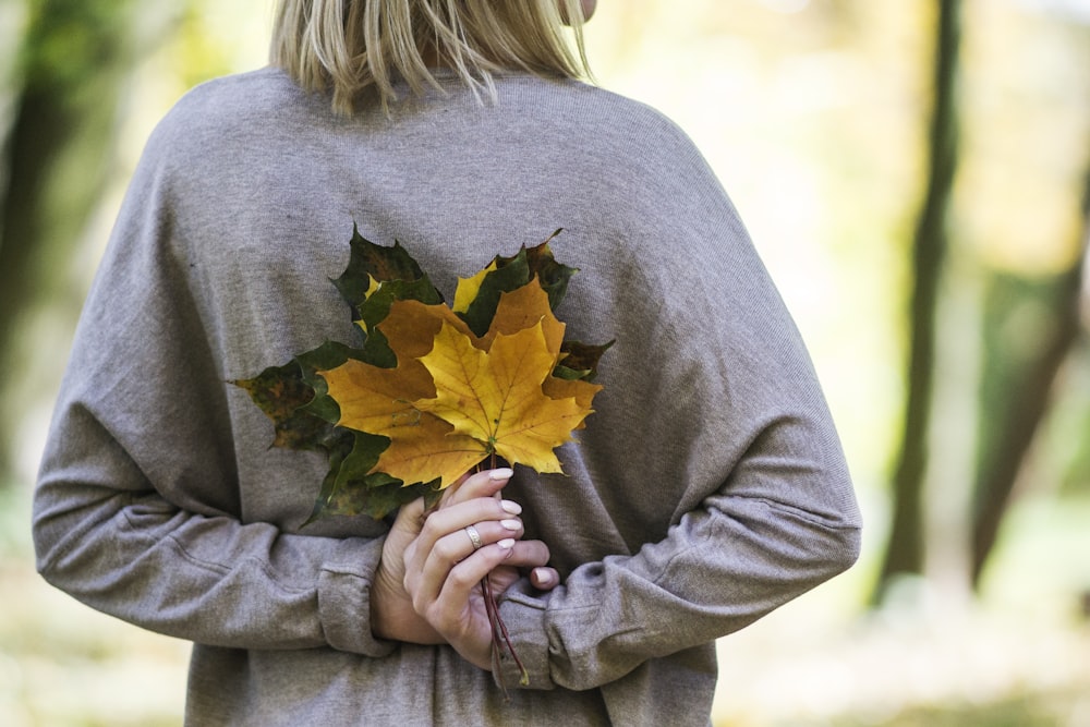 woman holding yellow and gray leaves during daytime