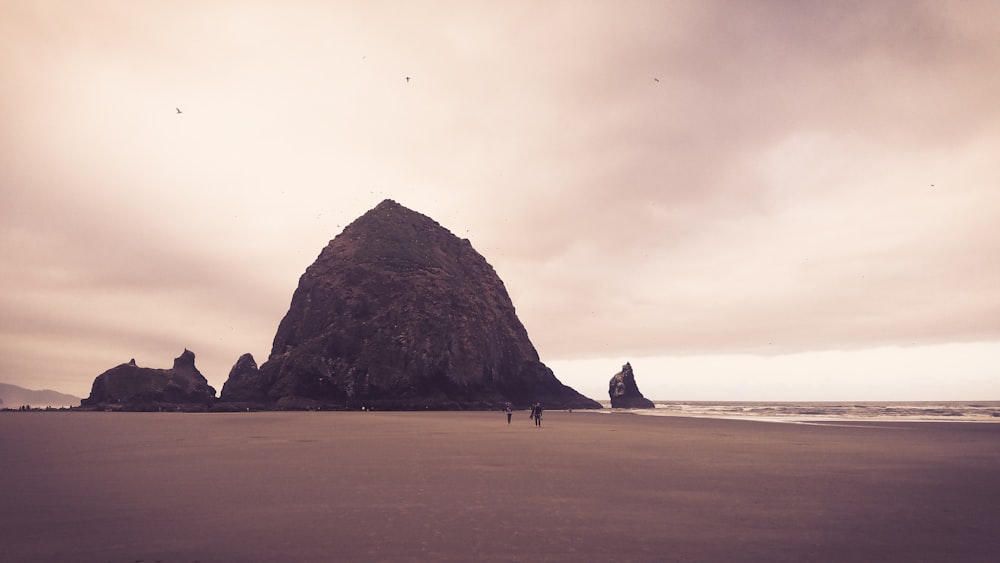 two persons walking on sand near mountain