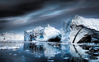 snow capped mountain near body of water under gray clouds