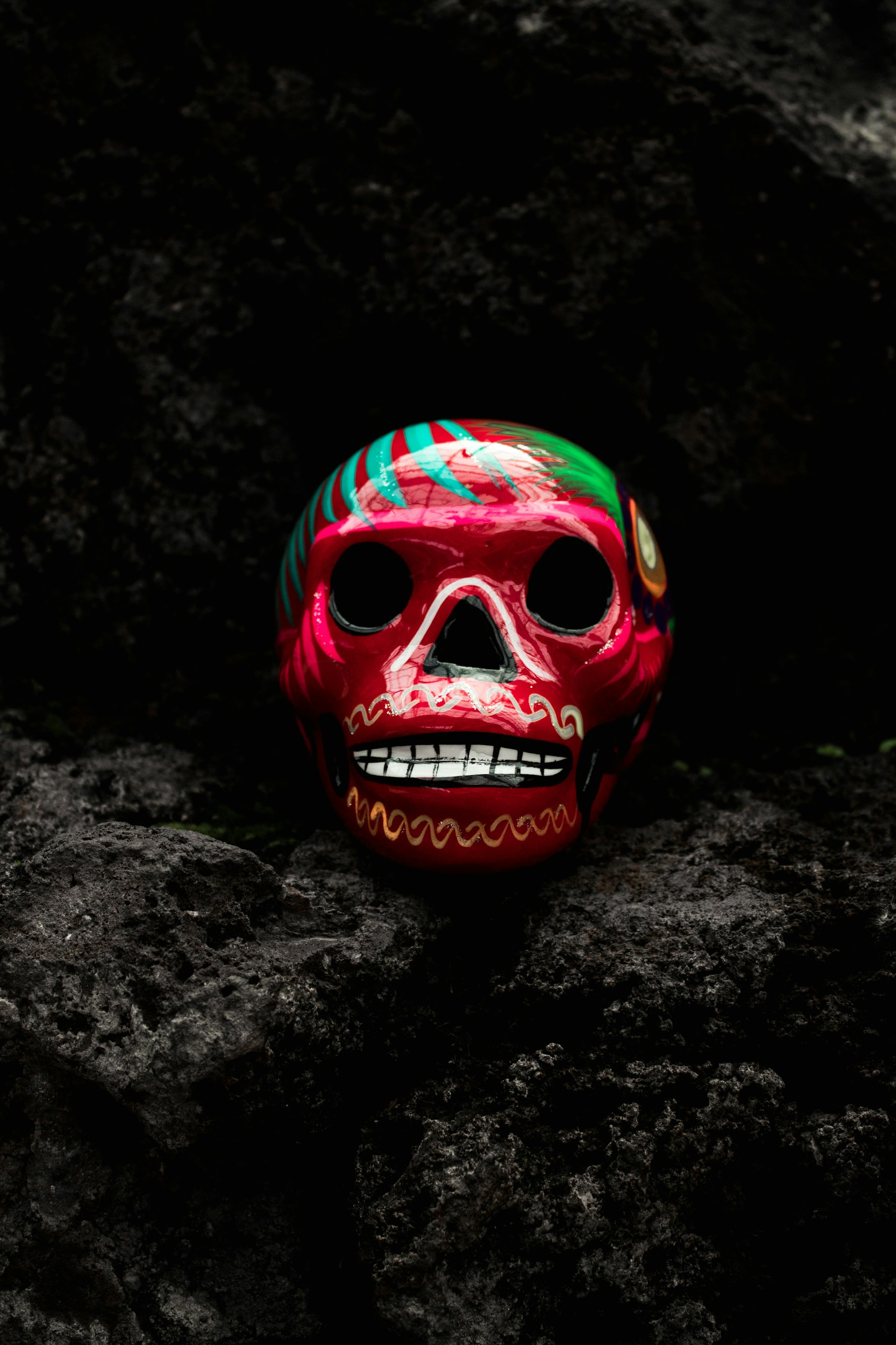 red and green ceramic skull ornament on black rock