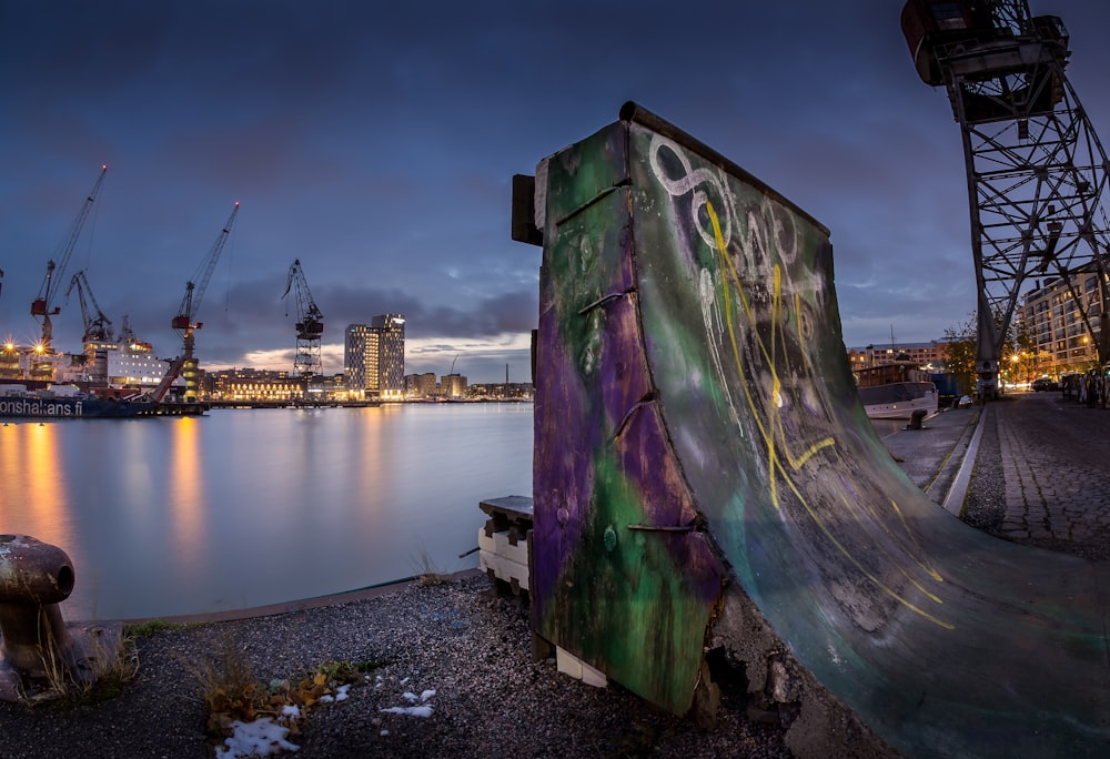 close-up photography of multicolored skateboard ramp near calm water at night time