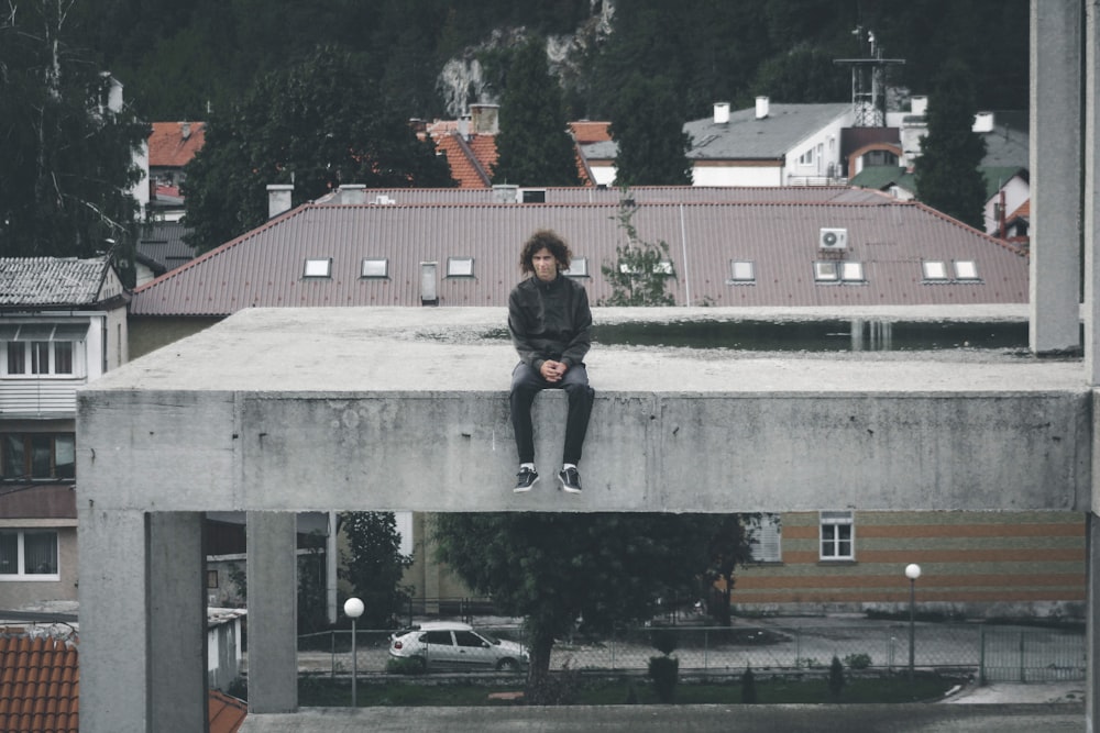 man wearing black jacket sitting on gray concrete