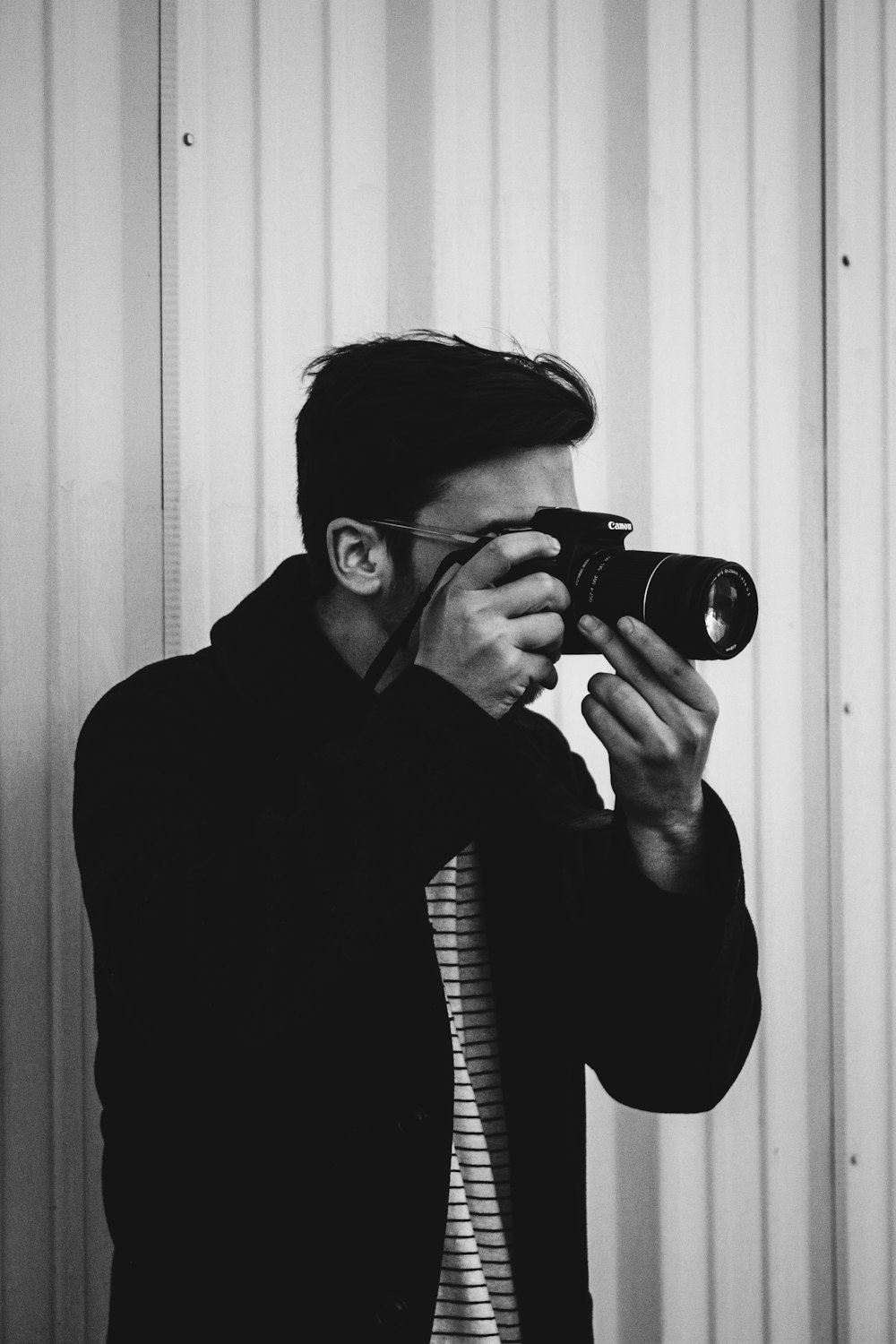 grayscale photograph of man holding DSLR camera while taking photo