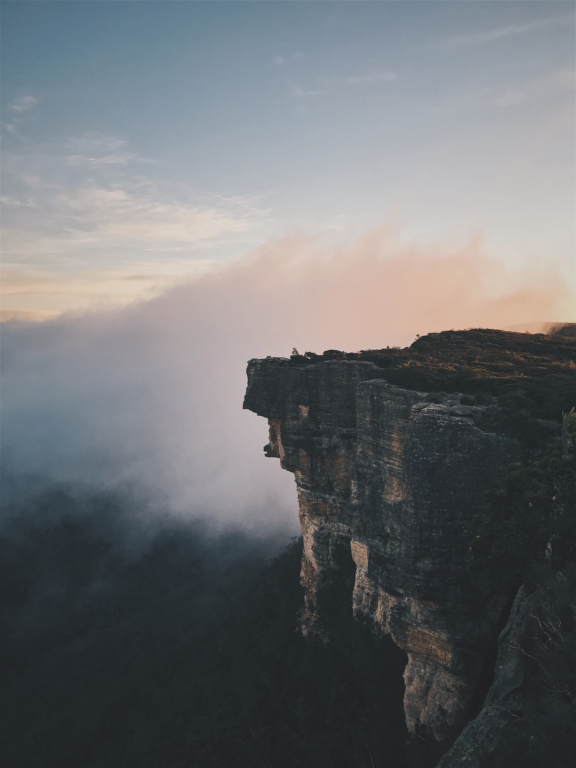 Hiker sitting on a mountain ledge at sunset, backpack beside them