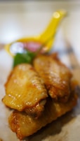Close-up view of succulent, golden-brown chicken wings arranged on a plate, with a small bowl of red dipping sauce in the background. The focus is on the wings, highlighting their appetizing texture and color.