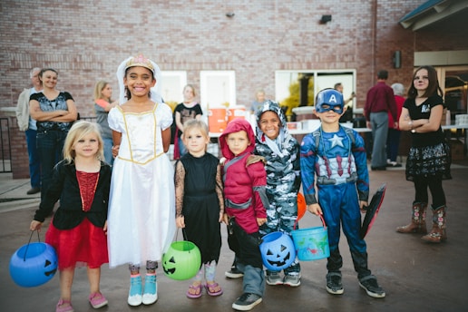 children standing while holding Jack 'o lantern and wearing costume