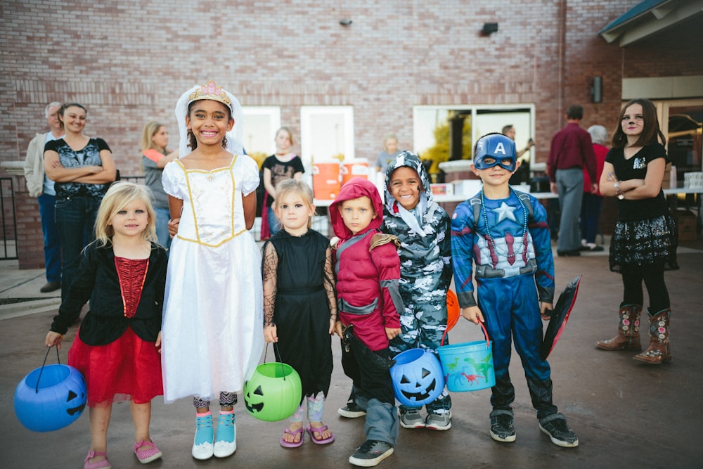 children standing while holding Jack 'o lantern and wearing costume