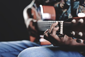 A close-up of hands playing a guitar with music notes in the background.