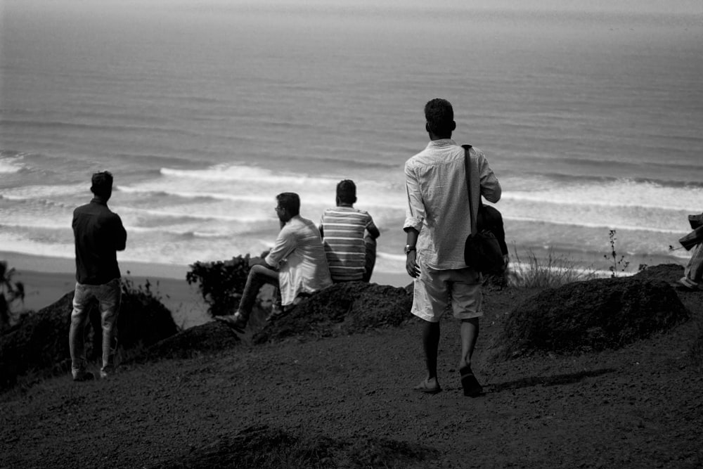 Foto en escala de grises de una persona caminando y mirando hacia la orilla del mar