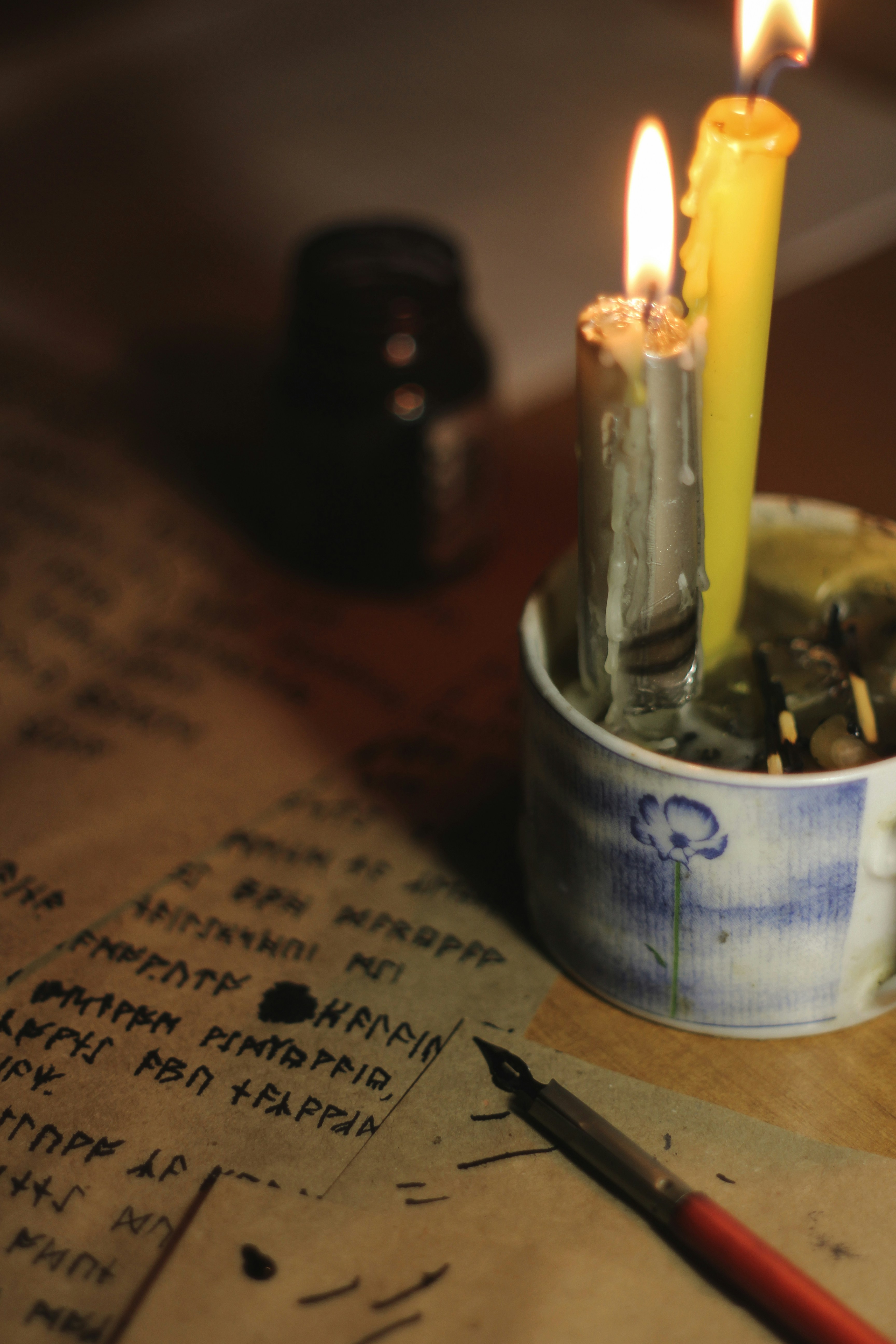 Handwritten letter on aged parchment paper beside ink pen, dim warm lamp light, deep shadows, quiet solitude