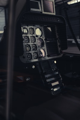 A close-up view of an aircraft cockpit featuring various dials, gauges, and electronic screens. The arrangement is dominated by analog instruments with circular displays and knobs. The lighting is dim, providing a moody and technical atmosphere.