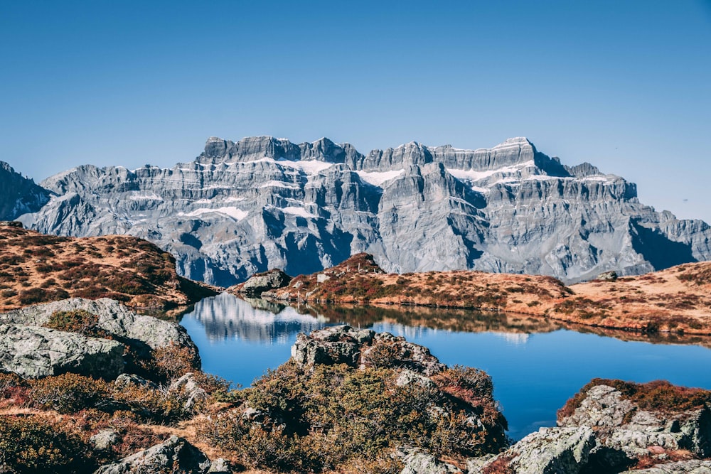 body of water near gray rocky mountain under blue sky