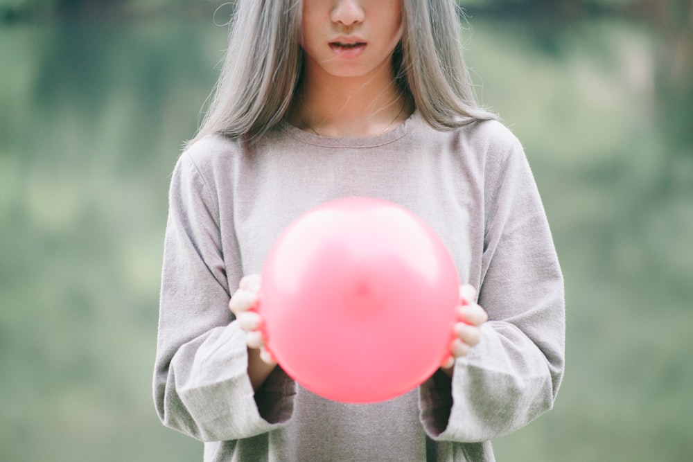 girl in grey long-sleeved shirt holding pink balloon