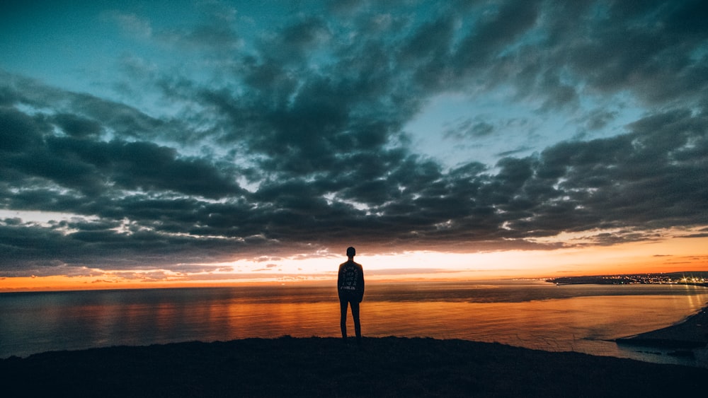 ゴールデンアワーに海の前に立つ人のシルエット写真