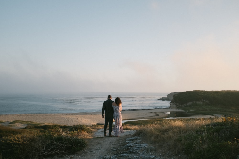 a man and woman standing on a path near the ocean