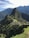 A panoramic view of the ancient Inca city of Machu Picchu, situated on a mountainous ridge with dramatic peaks and lush greenery surrounding the stone ruins. Terraced fields and stone structures are clearly visible, illustrating the historical and architectural significance of the site.
