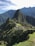 A panoramic view of the ancient Inca city of Machu Picchu, situated on a mountainous ridge with dramatic peaks and lush greenery surrounding the stone ruins. Terraced fields and stone structures are clearly visible, illustrating the historical and architectural significance of the site.