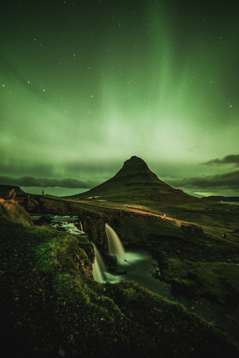 waterfalls near mountain taken under green sky