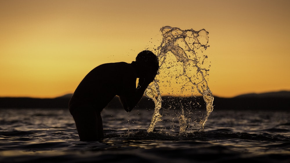 silhouette of man washing his face on body of water