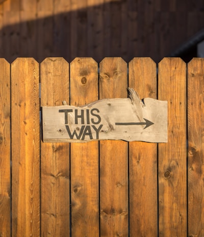 brown wooden plank fence with this way signboard