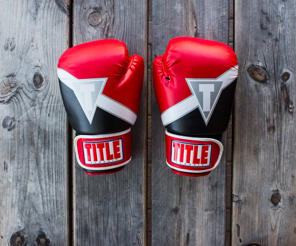 par de guantes de entrenamiento Title rojos y negros sobre tablón de madera gris