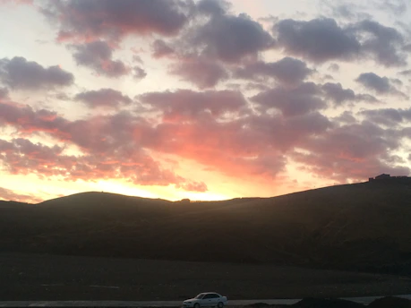 A vibrant sunset over a winding mountain road with a colorful van parked at the side.