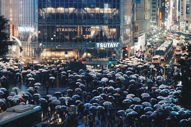 A bustling Shibuya crossing filled with colorful umbrellas under a soft rain.