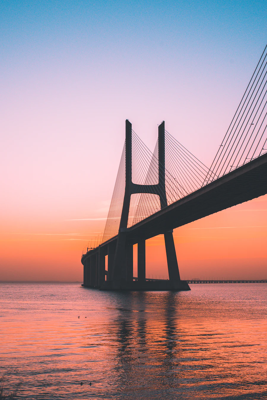 Cable-stayed bridge silhouette against a warm sunset sky