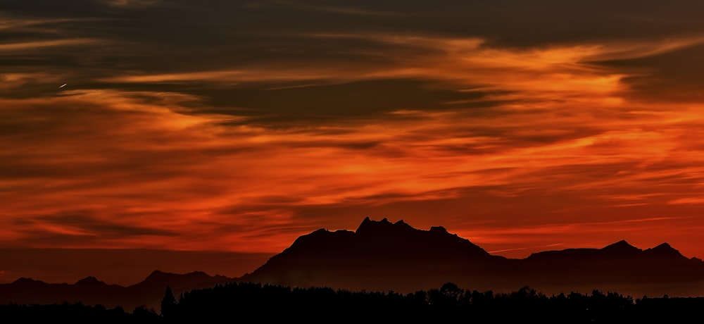 silhouette on mountain during red sky