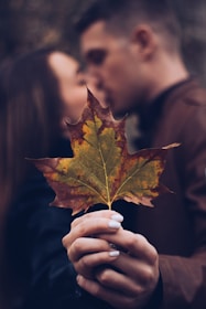 man and woman holding leaf while kissing
