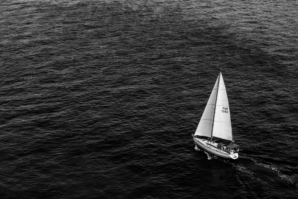 fotografia in scala di grigi della barca a vela sullo specchio d'acqua