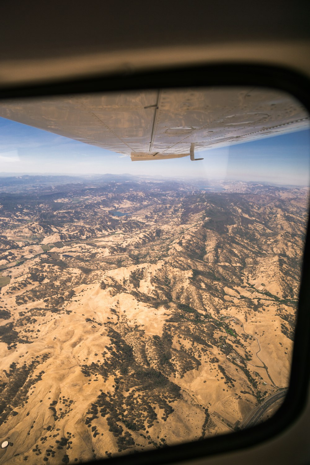 white plane wing above brown hills at daytime