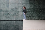 A person stands on the edge of a polished floor near a reflective water surface. The background features large green marble tiles with a natural pattern.