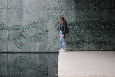 A person stands on the edge of a polished floor near a reflective water surface. The background features large green marble tiles with a natural pattern.
