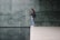 A person stands on the edge of a polished floor near a reflective water surface. The background features large green marble tiles with a natural pattern.