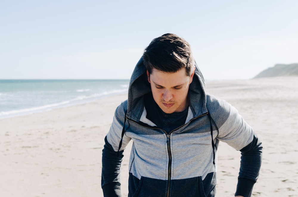 man in gray and black zip-up hoodie walking beside ocean