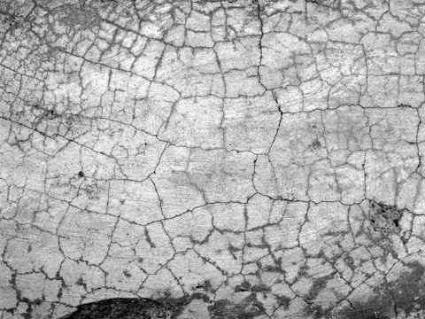 A textured surface with a network of intricate cracks forming a web-like pattern across the entire area. The surface appears weathered and aged, suggesting erosion or wear over a significant period.