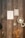 A wooden wall features two framed prints with motivational text, a modern wall lamp, and decorative ceramic plates. Bright orange branches provide a pop of color at the bottom.