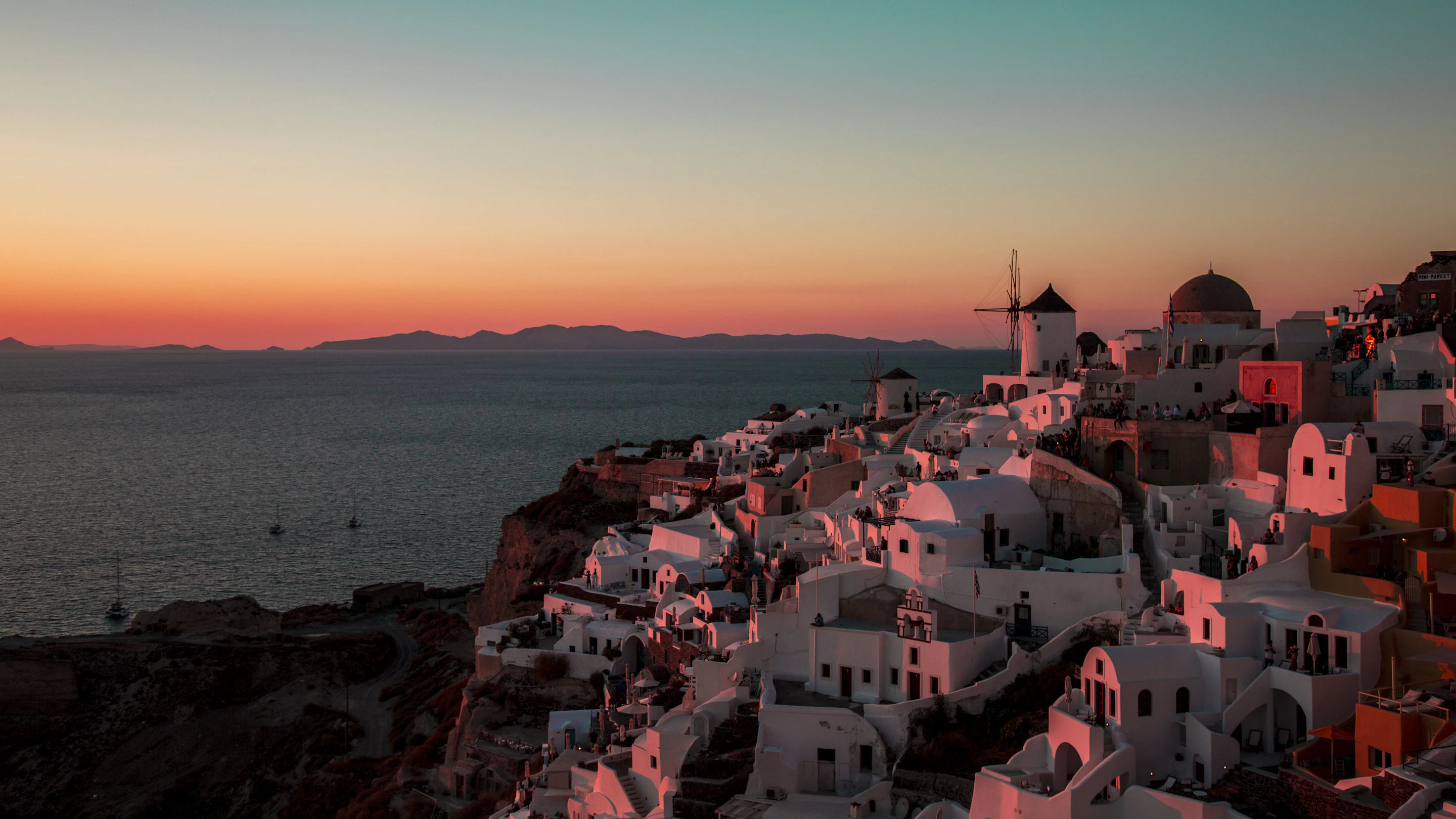 Oia on Santorini at sunset, its white and pastel houses glowing on the caldera cliffs above the Aegean