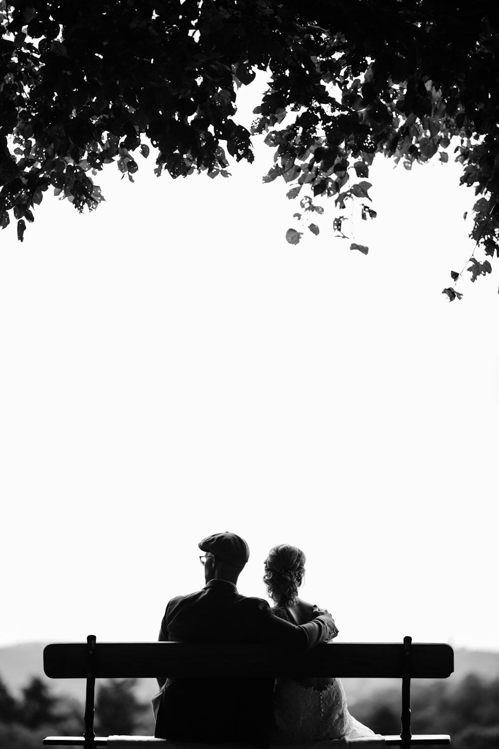 couple assis sur un banc sous la photographie en niveaux de gris d’un arbre