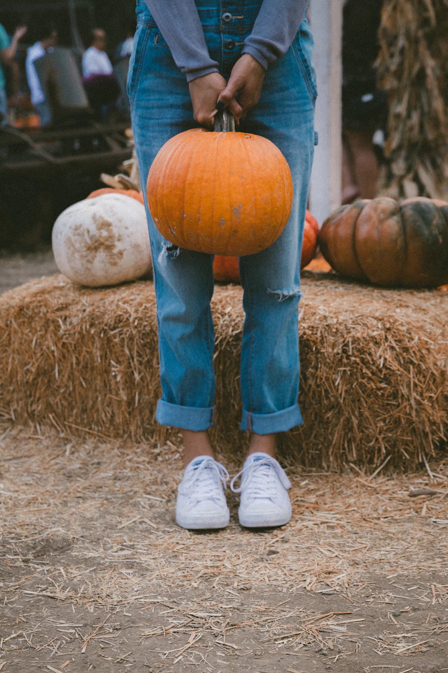 A woman carrying a pumpkin beside hay bales