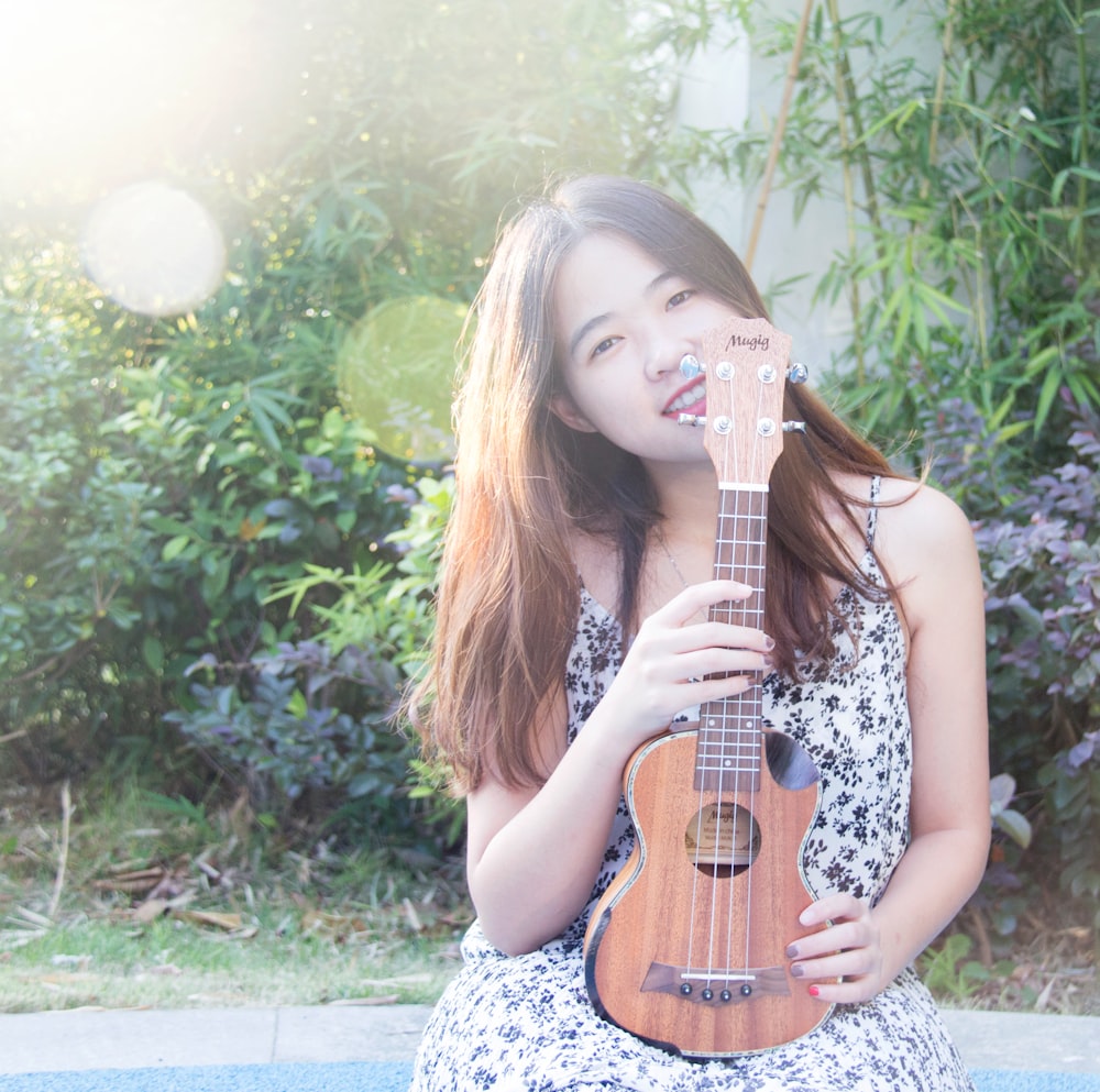smiling woman holding ukulele near green plants