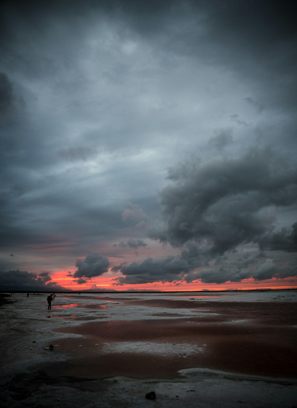 a couple of people standing on top of a beach under a cloudy sky