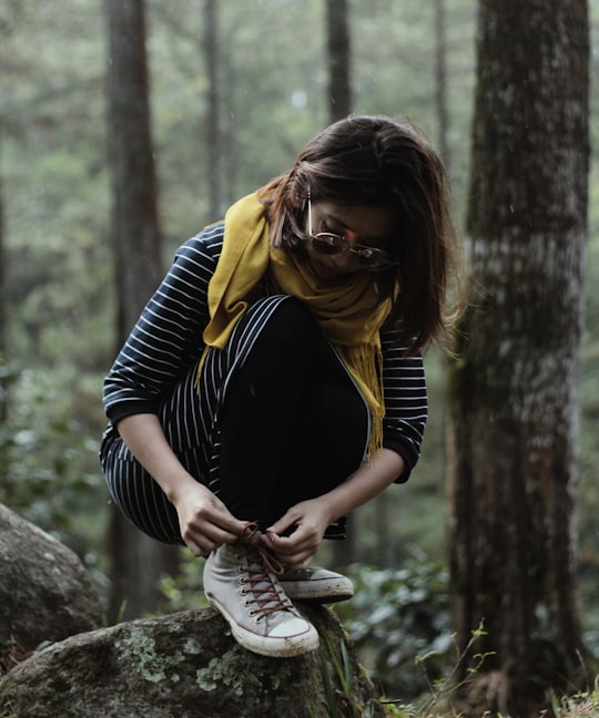 woman lacing her shoes while on top of stone near tall trees in Bandung Indonesia