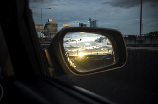 A sleek car side mirror reflecting a vibrant city street at sunset.