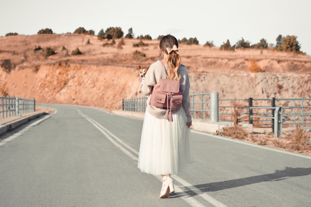 woman walking on asphalt road while carrying brown and white dog