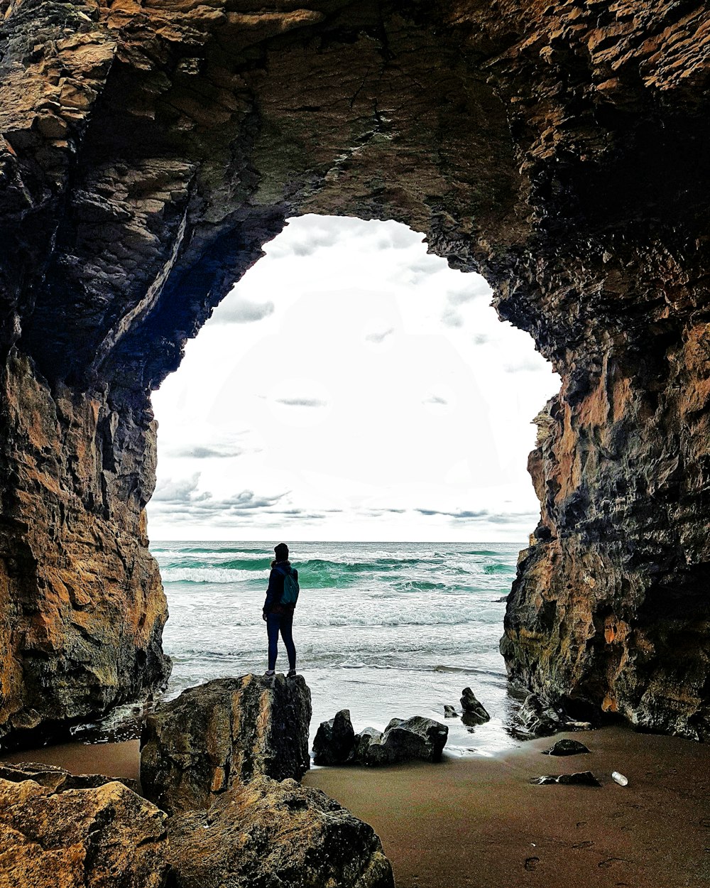 homme en veste noire debout sur une formation rocheuse près de la mer pendant la journée