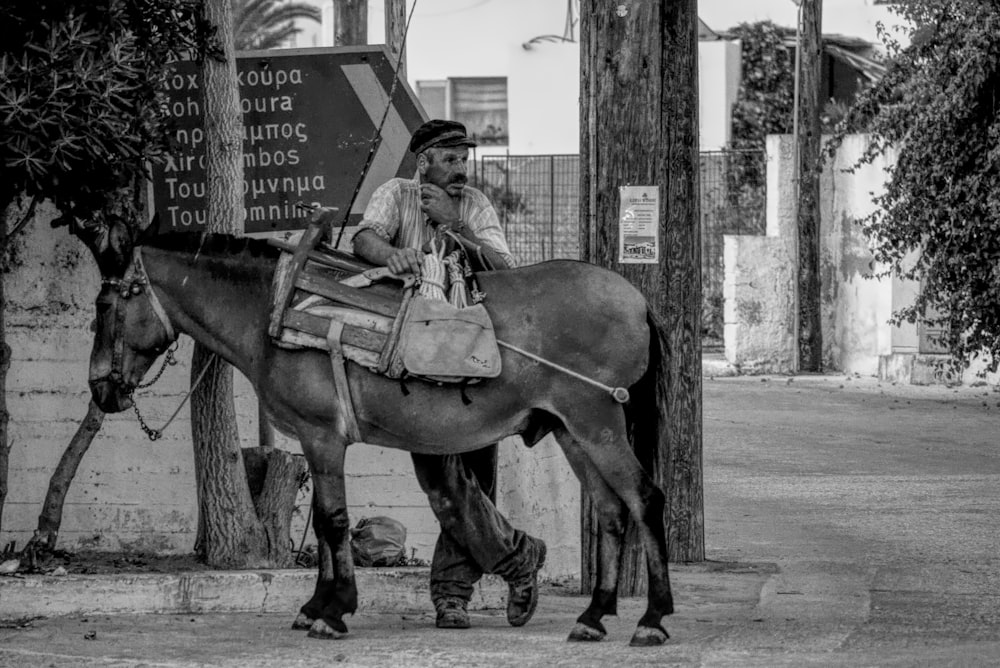 grayscale photography of man standing beside horse