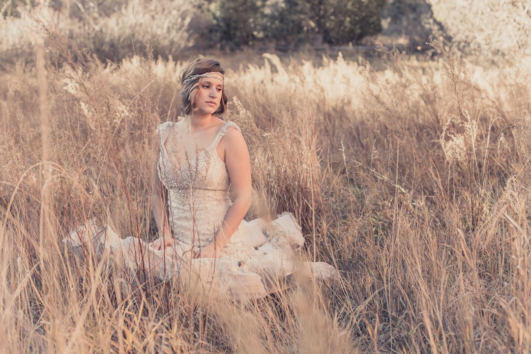 woman wearing white lace sleeveless mermaid dress while sitting on wilted grass